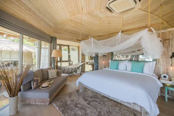 Schlafzimmer im Treehouse Villas Koh Yao mit Holzdecke, Bett, Hängebett und großer Fensterfront.