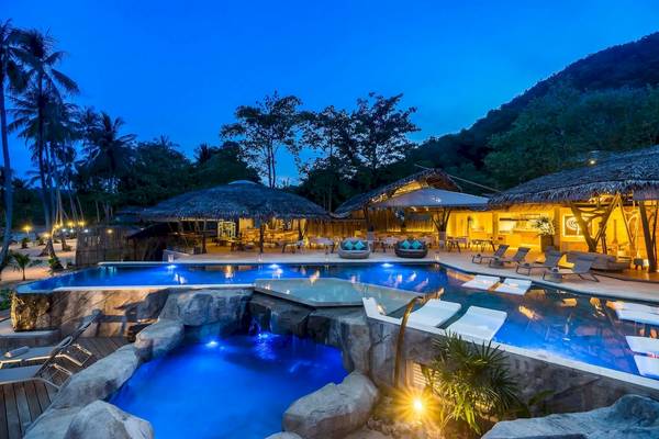 Der Pool der TreeHouse Villas Koh Yao bei Nacht mit blauem Licht und Liegestühlen.