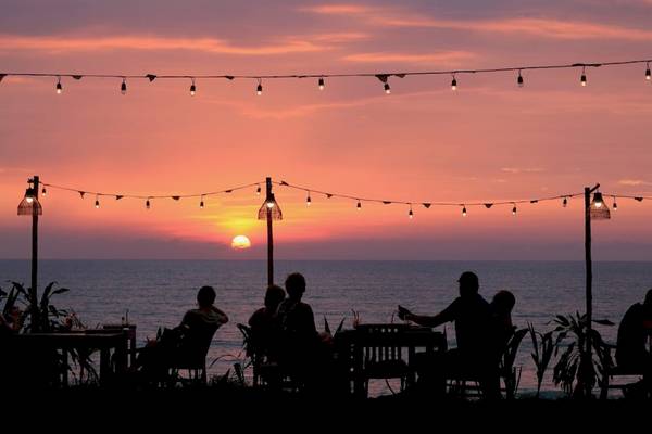 Menschen sitzen bei Sonnenuntergang am Meer auf einem Tisch im Freien des Haadson Resorts.