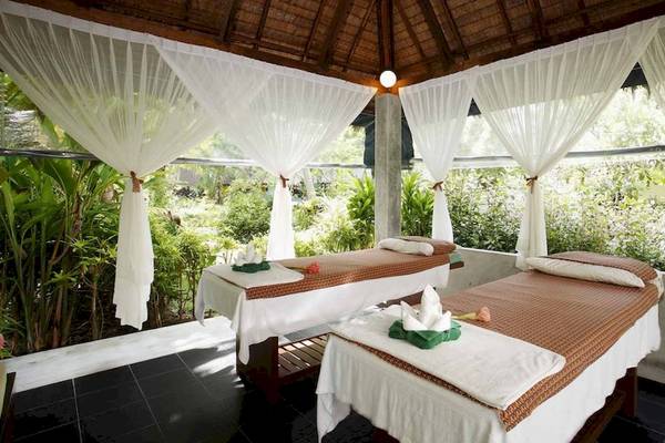 Massagebehandlungsraum im Haadson Resort mit zwei Massagetischen, weißen Vorhängen und grünen Pflanzen im Hintergrund.