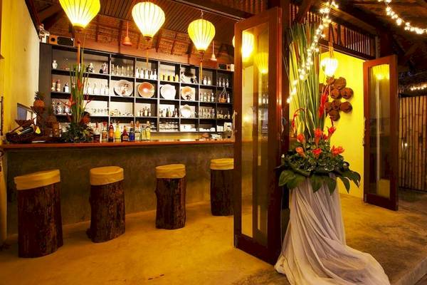 Innenansicht der Bar im Haadson Resort mit gelben Wänden, Holzbarhockern und blumiger Dekoration.