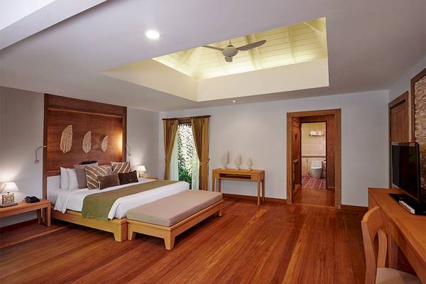 Innenansicht eines Zimmers im Khaolak Paradise Resort mit großem Bett, Holzboden und Glasfenstern.
