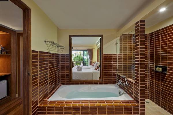 Badezimmer im Khaolak Paradise Resort mit Badewanne und Spiegel, der ein Schlafzimmer zeigt.