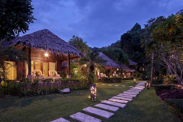 Außenansicht des Khaolak Paradise Resorts bei Nacht mit beleuchteten Hütten und einem gepflasterten Weg.