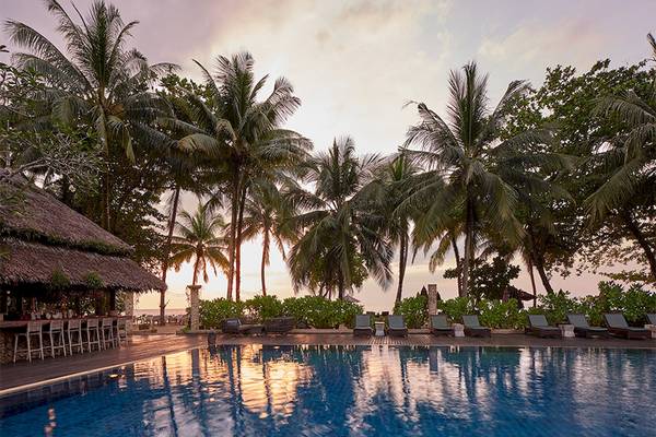 Ein Swimmingpool im Khaolak Paradise Resort bei Sonnenuntergang mit Palmen und Sonnenliegen.