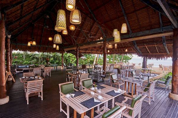 Das Esszimmer des Khaolak Paradise Resorts mit Holztischen und Stühlen, hängenden Laternen und Blick auf den Strand.