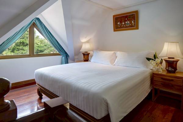 Schlafzimmer im Santiburi Koh Samui Hotel mit Bett, Lampen und Fenstern.