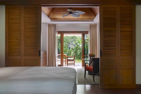 Schlafzimmer im Santiburi Koh Samui Hotel mit Blick auf den Garten und Außenmöbeln.