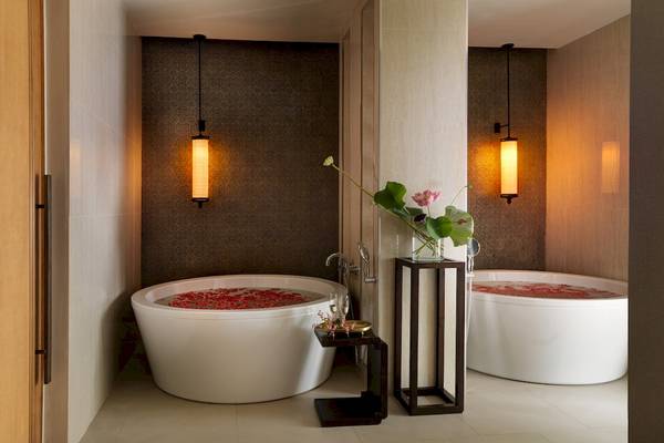 Luxuriöses Badezimmer im Santiburi Koh Samui Hotel mit zwei Badewannen, Blumen und Beleuchtung.