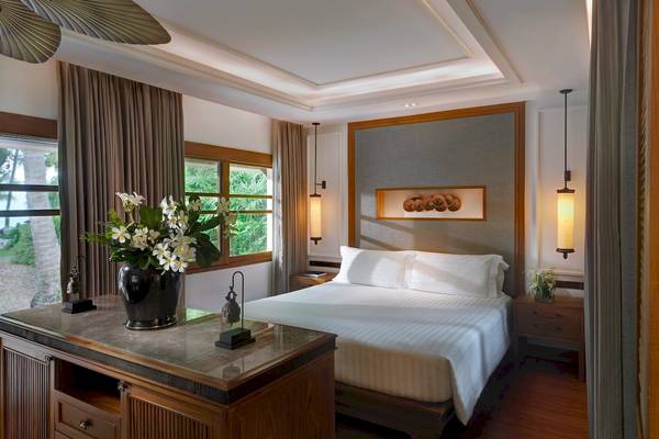 Schlafzimmer im Santiburi Koh Samui Hotel mit Doppelbett, Blumenvase und Fenstern.
