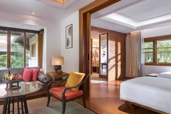 Innenansicht eines Zimmers im Santiburi Koh Samui Hotel mit Bett, Couch, Tisch, Lampe und Fenstern.