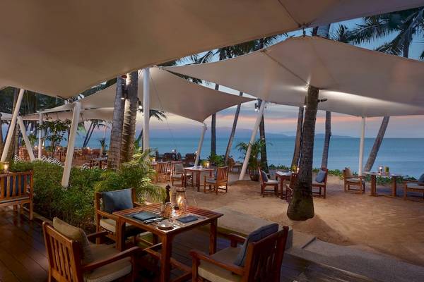 Außenbereich des Santiburi Koh Samui Hotels mit Sonnenschirmen und Tisch am Strand.