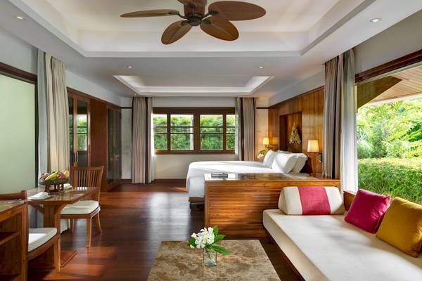 Innenansicht eines Zimmers im Santiburi Koh Samui Hotel mit Bett, Tisch und Fenstern.