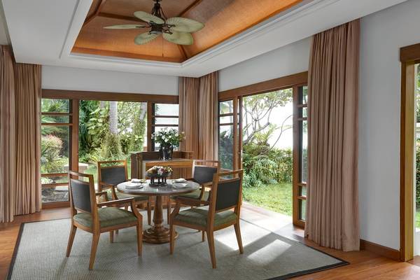 Gartensitzecke des Santiburi Koh Samui Hotels mit Tisch und Stühlen, umgeben von großen Fenstern und Pflanzen.