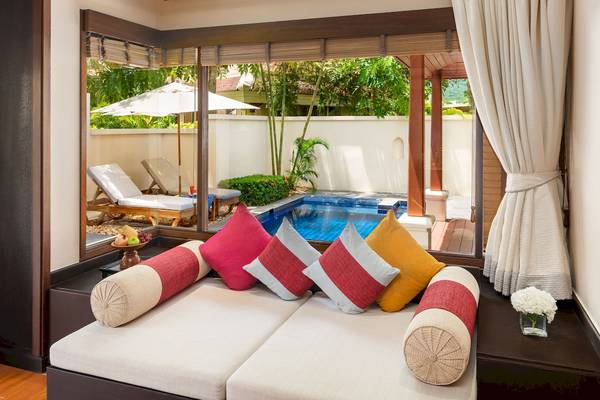 Sofa im Hotelzimmer mit Aussicht auf Pool, Lounge-Stühle und ein Schirm draußen.