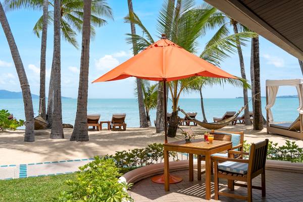 Santiburi Koh Samui Strand mit Tisch unter einem orangefarbenen Sonnenschirm.