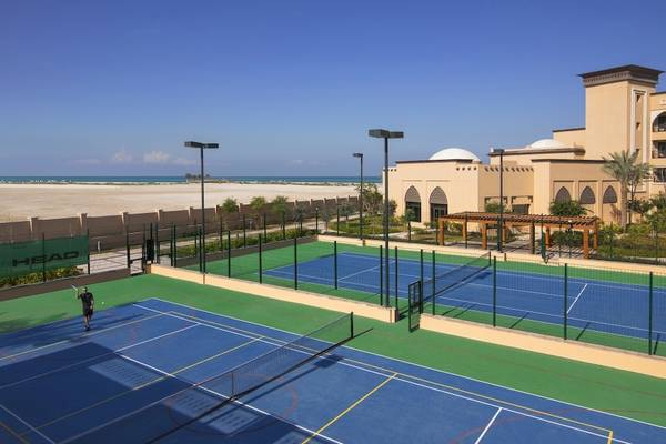 Tennisplatz im Saadiyat Rotana Resort & Villas mit Blick auf das Meer und eine Person, die spielt.