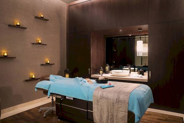 Spa-Behandlungsraum im Saadiyat Rotana Resort & Villas mit Behandlungsliege, Waschbecken und Spiegel.