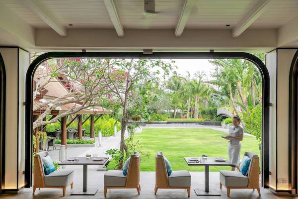 Außenbereich des Meliá Koh Samui Hotels mit Tischen und Stühlen und Blick auf eine Frau und eine Rasenfläche.