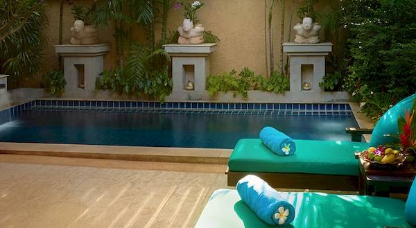 Poolbereich des Bo Phut Resort & Spa mit zwei grünen Liegen und blauen Kissen, umgeben von Pflanzen und Dekofiguren.