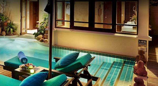 Pool-Terrasse im Bo Phut Resort & Spa mit grünen Liegestühlen und einem kleinen Tisch.