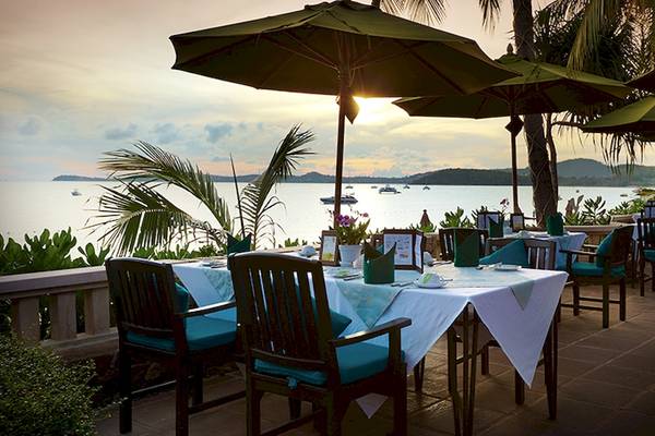 Außenbereich des Bo Phut Resort & Spa mit Tischen und Stühlen unter grünen Sonnenschirmen mit Blick auf das Meer.
