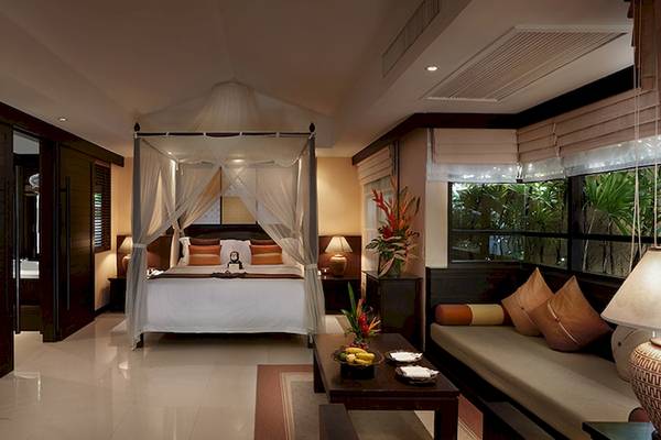 Innenansicht des Schlafzimmers im Bo Phut Resort & Spa mit Himmelbett, Pflanzen und Sofa.