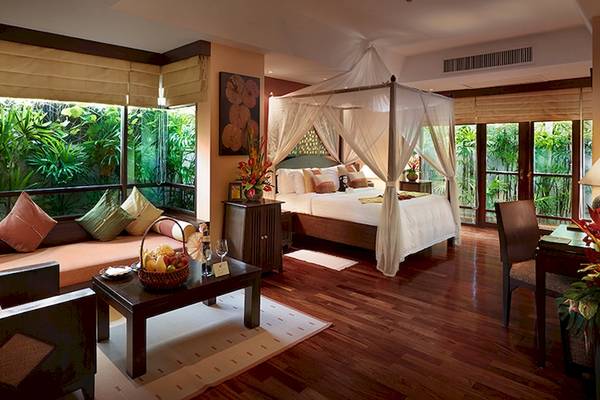 Schlafzimmer im Bo Phut Resort & Spa mit einem großen Bett unter einem Baldachin, Fenstern mit Jalousien und Blick auf den Garten.