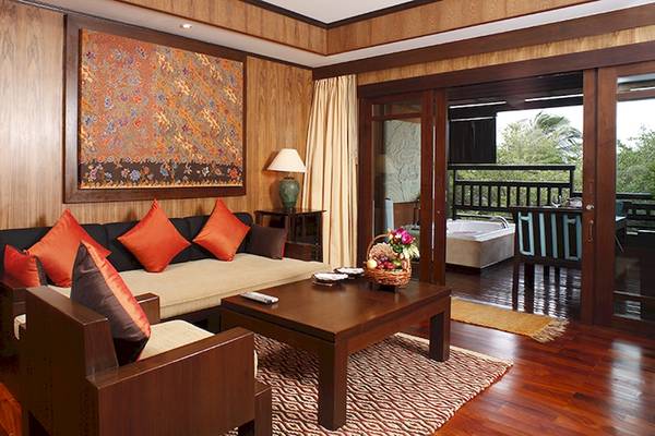 Wohnzimmer im Bo Phut Resort & Spa mit Holzmöbeln, einem großen Wandteppich und einem Balkon mit Blick auf einen Whirlpool.