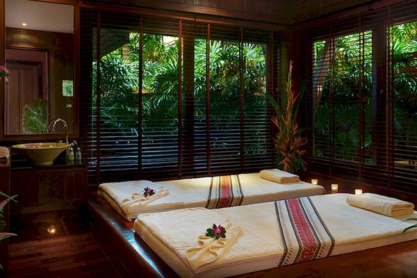 Massageraum im Bo Phut Resort & Spa mit zwei Betten, Fenstern und Pflanzen im Hintergrund.