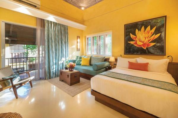 Hotelzimmer im Buri Rasa Village Samui mit gelben Wänden, großer Liegefläche und Balkon.