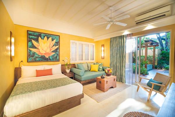 Ein hellgelbes Zimmer im Buri Rasa Village Samui Hotel mit einem Bett, Sofa, Tisch und Gartenblick.