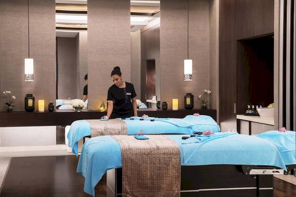 Massagebereich im Saadiyat Rotana Resort mit zwei Massagetischen und einer Frau, die die Betten vorbereitet.