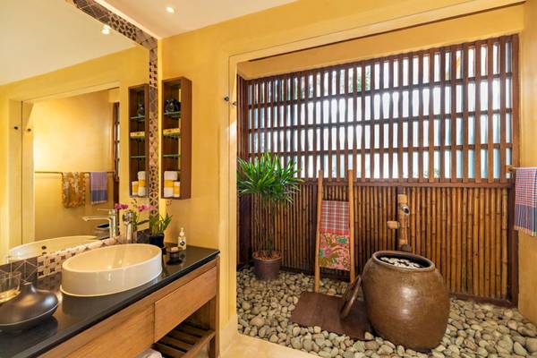 Badezimmer im Buri Rasa Village Samui Hotel mit gelben Wänden, einem Waschbecken, Spiegel und Bambuswänden.