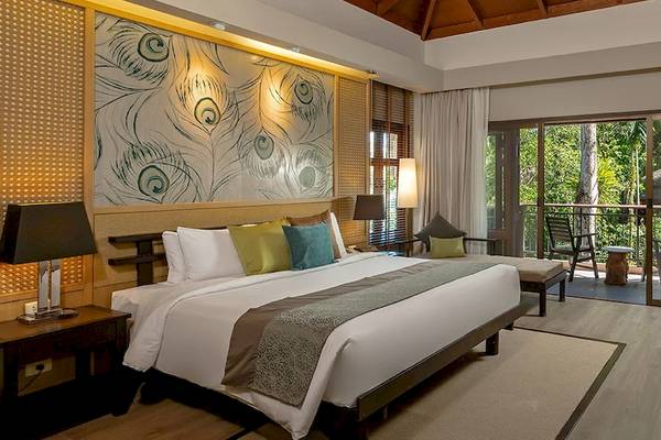 Innenansicht eines Zimmers im Khao Lak Merlin Resort Hotel mit großem Bett, dekorativer Wand, Balkon und Panoramafenstern.