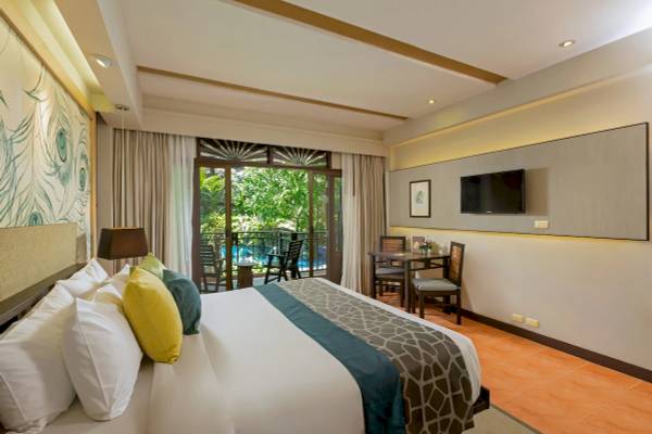 Innenansicht eines Zimmers im Khao Lak Merlin Resort mit einem großen Bett, Kissen, Balkon und Außenpoolsicht.