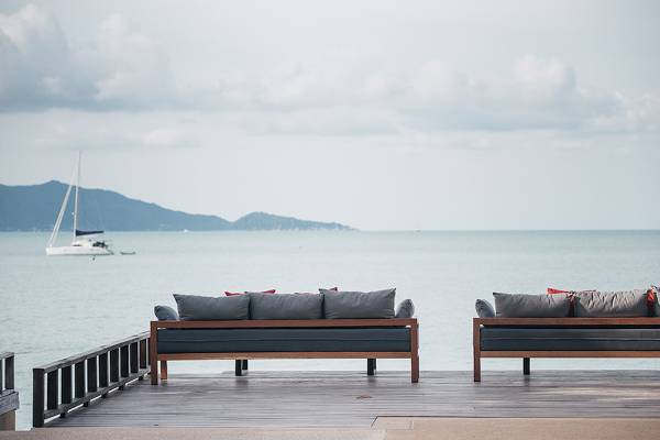 Zwei Loungesofas am Wasser im Peace Resort mit Blick auf das Meer und eine Segelyacht.