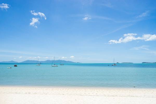 Friedlicher Strand mit Booten im Wasser und Bergen im Hintergrund.