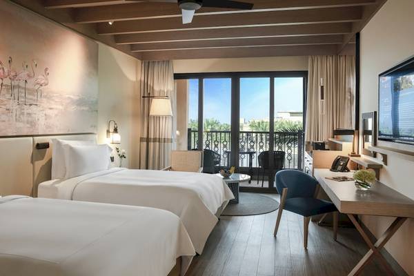 Hotelzimmer im Saadiyat Rotana Resort & Villas mit zwei Betten, einem Schreibtisch und einem Balkon.