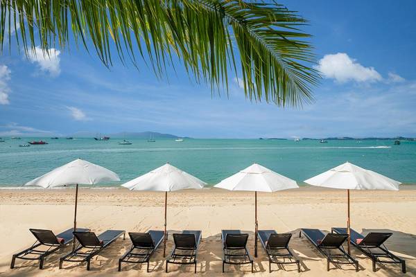 Strand mit Sonnenliegen und Sonnenschirmen, Blick auf das Meer und einige Boote in der Ferne.
