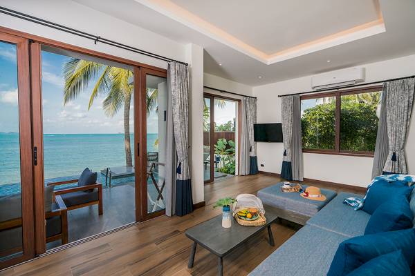 Wohnzimmer des Peace Resort mit Meerblick, blauem Sofa und Glastüren, die zu einem Pool führen.