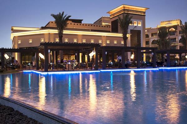 Abendansicht des Saadiyat Rotana Resort & Villas mit beleuchtetem Pool und Gästen.