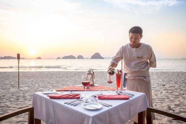 Ein Kellner serviert ein Getränk an einem gedeckten Tisch am Strand des Tup Kaek Sunset Beach Resorts.