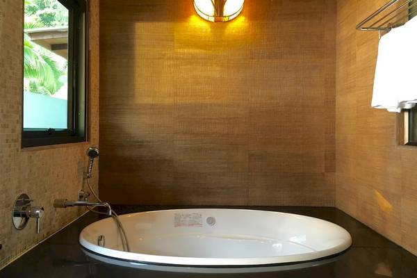 Badezimmer des Tup Kaek Sunset Beach Resorts mit einer Badewanne, einer Wand aus Holzimitat und einem Fenster.