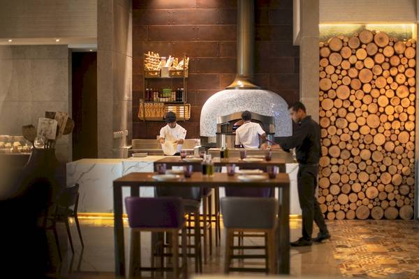 Im Restaurant des Saadiyat Rotana Resort & Villas stehen Köche vor einem Ofen, während ein Gast serviert wird.