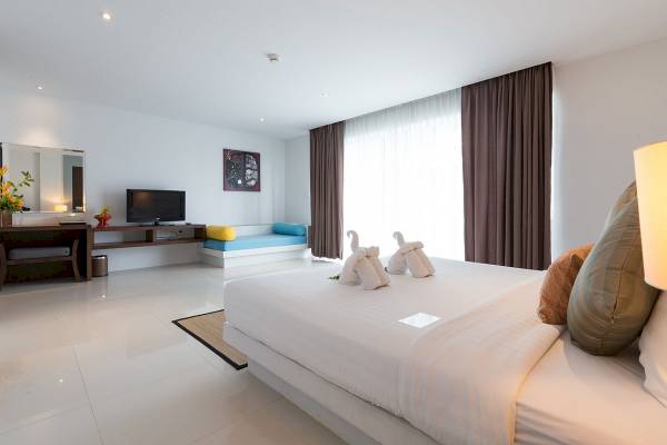 Schlafzimmer im Peace Laguna Resort & Spa mit weißem Bett, Fernseher und Fenstervorhängen.