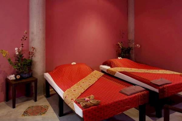 Zwei rote Betten im Spa-Bereich des Peace Laguna Resort & Spa mit roten Decken und Kissen, umgeben von roten Wänden und Blumen.
