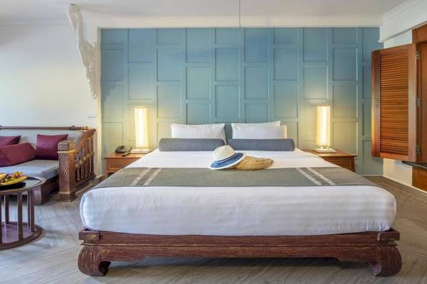 Ein modernes Hotelzimmer mit einem großen Bett, das von zwei Nachttischen flankiert wird, und einer blauen Wand mit einer Holzvertäfelung.