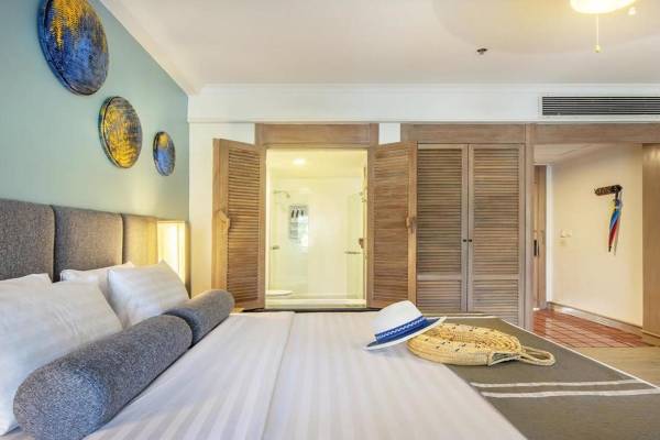 Ein modernes Hotelzimmer mit einem großen Bett, mehreren Kissen und Accessoires wie einem Hut und einer Tasche.