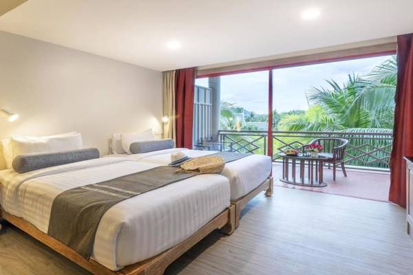 Zimmer im Chada Thai Village Resort mit zwei Betten und einem Balkon, der auf eine Terrasse mit Tisch und Stühlen führt.